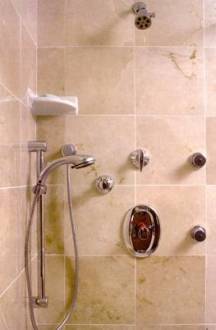 Shower featuring body sprays, hand held spray,  thermostat control valve, and tile walls with opposing clear glass panels and door.